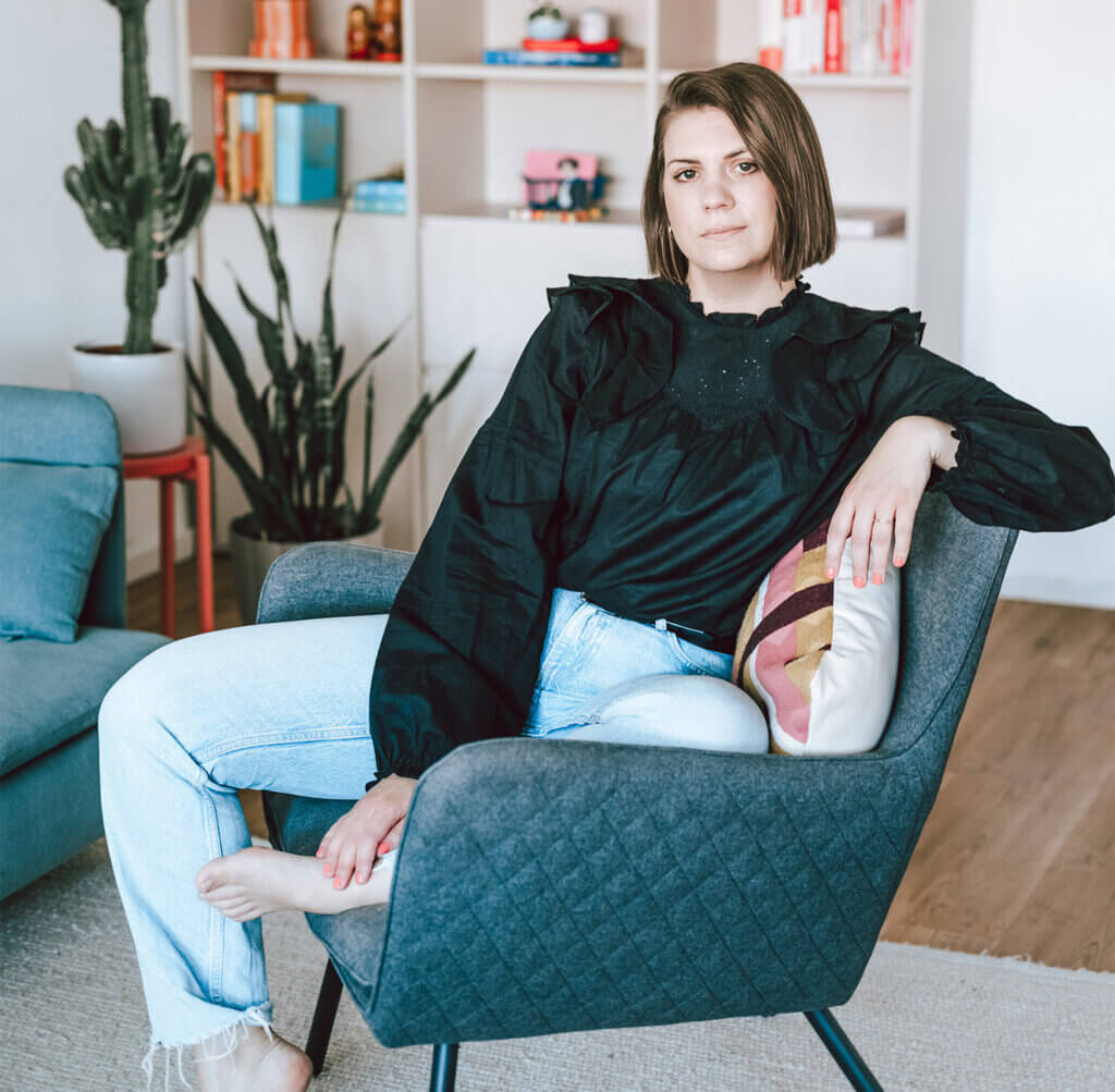 Frau sitzt auf einem Stuhl und schaut in die Kamera